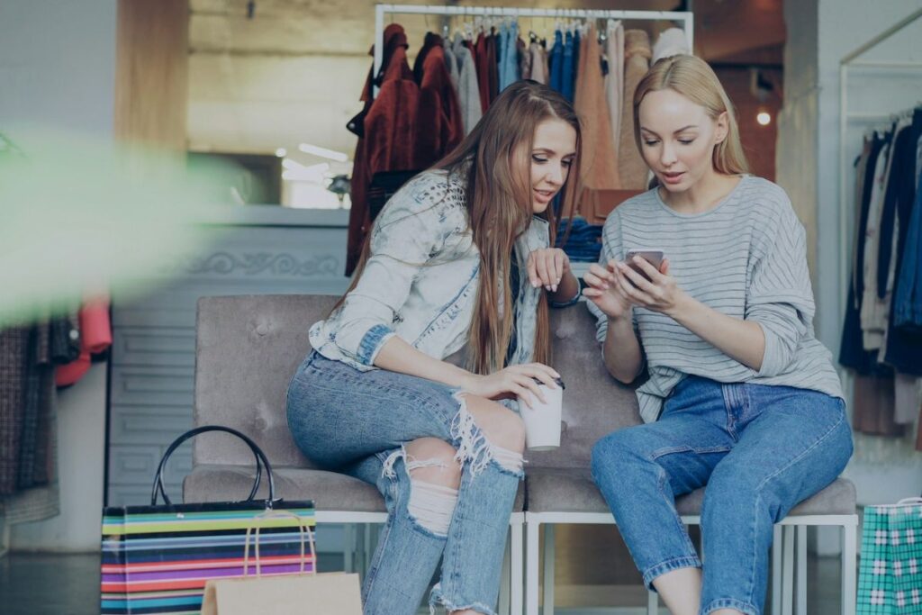 mulheres olhando celular com sacolas